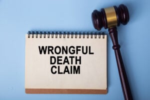 Gavel beside a notepad reading 'Wrongful Death Claim' on a blue surface, indicating legal proceeding.