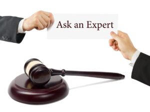 Two hands hold a white card reading 'Ask an Expert' above a judge's gavel in the foreground.