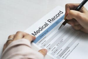 A person writes on a medical record form with a pen, capturing patient information.